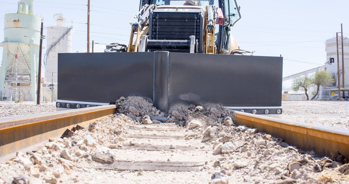 DymaxRail Rail Ballast Plow mounted on Cat 420F backhoe loader clearing spilled ballast on rail track