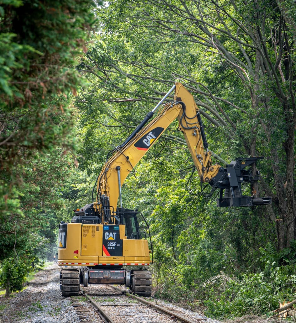 Cat excavator using Dymax 21" tree shear to trim branches overhanging railroad