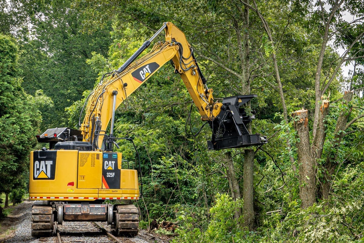 DymaxRail excavator tree shear mounted on Cat excavator cutting a large tree near railroad tracks