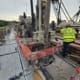 Close-up of DymaxRail cart with drilling equipment positioned directly over the dam deck during deep anchor shaft drilling.