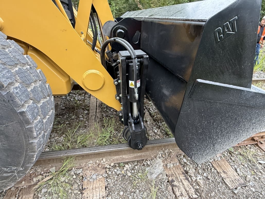 Bucket-mounted Dymax LoPro Rail Rider rail wheel assembly on a Caterpillar hi-rail backhoe