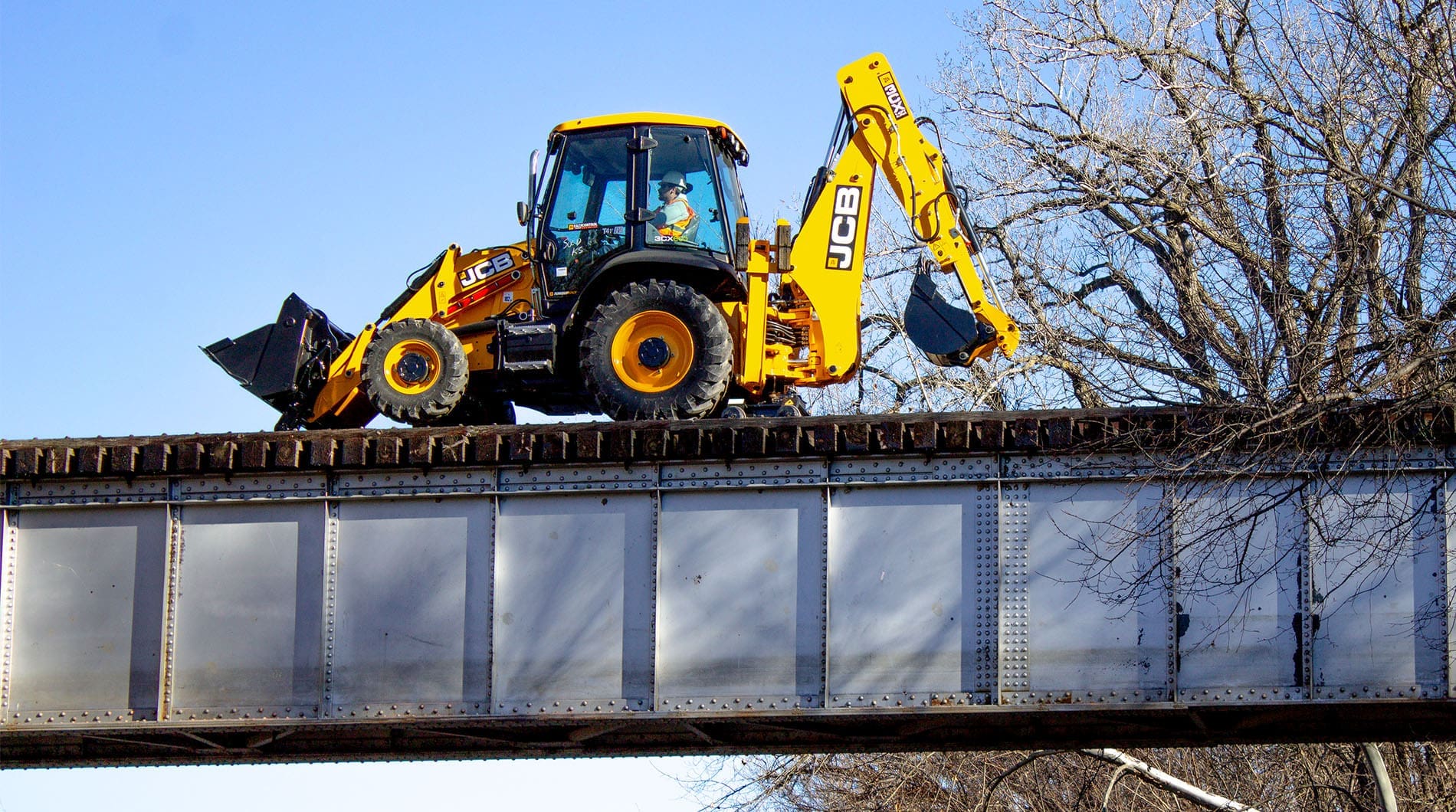Rail Rider hi-rail guide system for backhoes hero Backhoe loader equipped with the Dymax Rail Rider hi-rail guide system traveling on railroad track