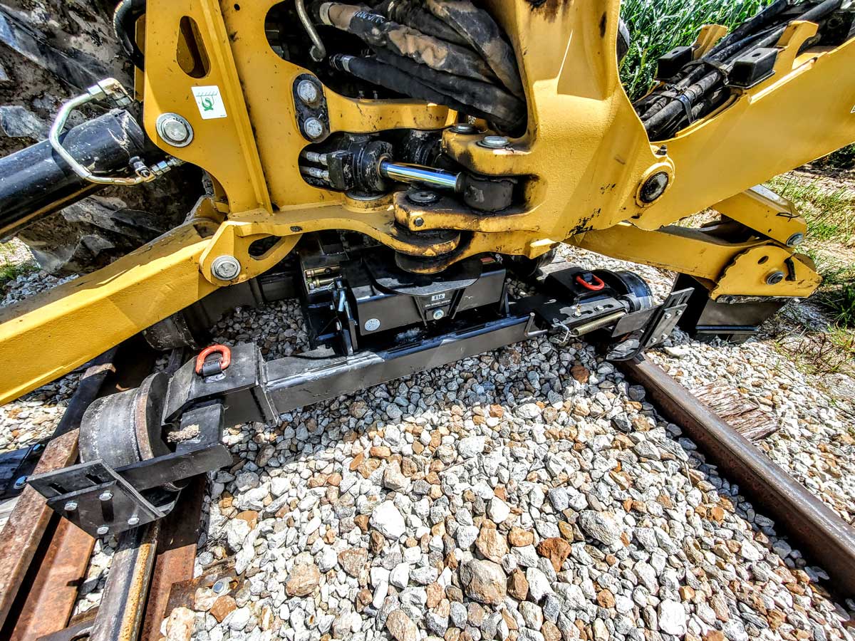 Close-up of the Dymax LoPro Rail Rider rear 4-wheel dolly mounted on a Caterpillar backhoe on rail