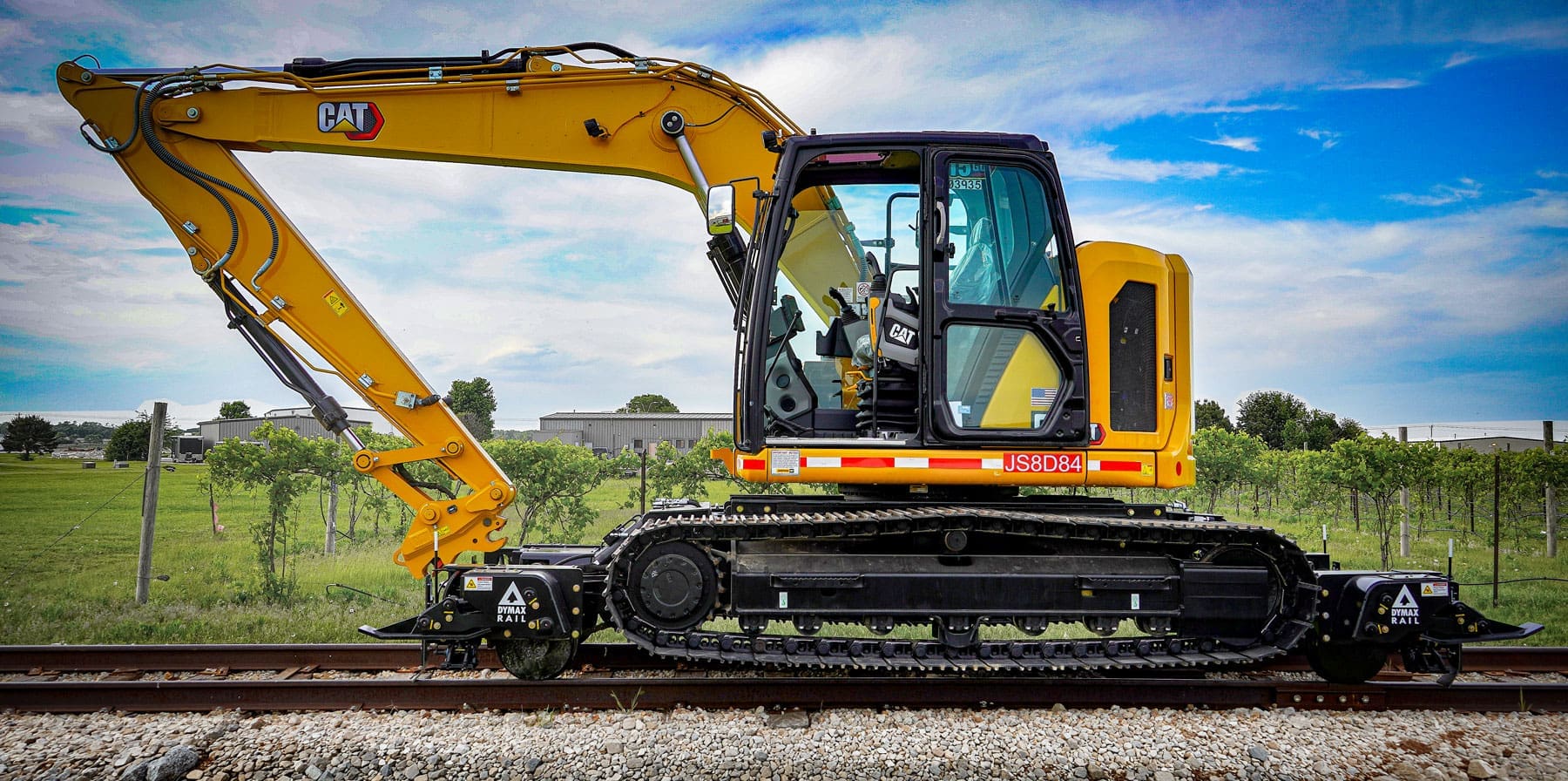 Cat 315 track excavator equipped with the Dymax Rail Rider X2-15T detachable hi-rail attachment on rail in an open field