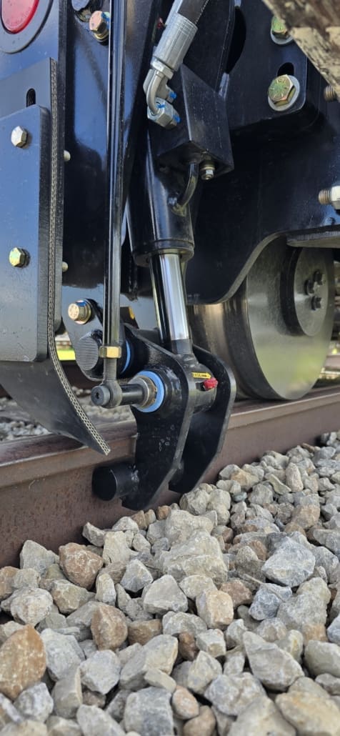 Close-up of the Dymax Rail Rider X2 hydraulic rail clamp engaged on the rail head, locking the hi-rail system in position for work