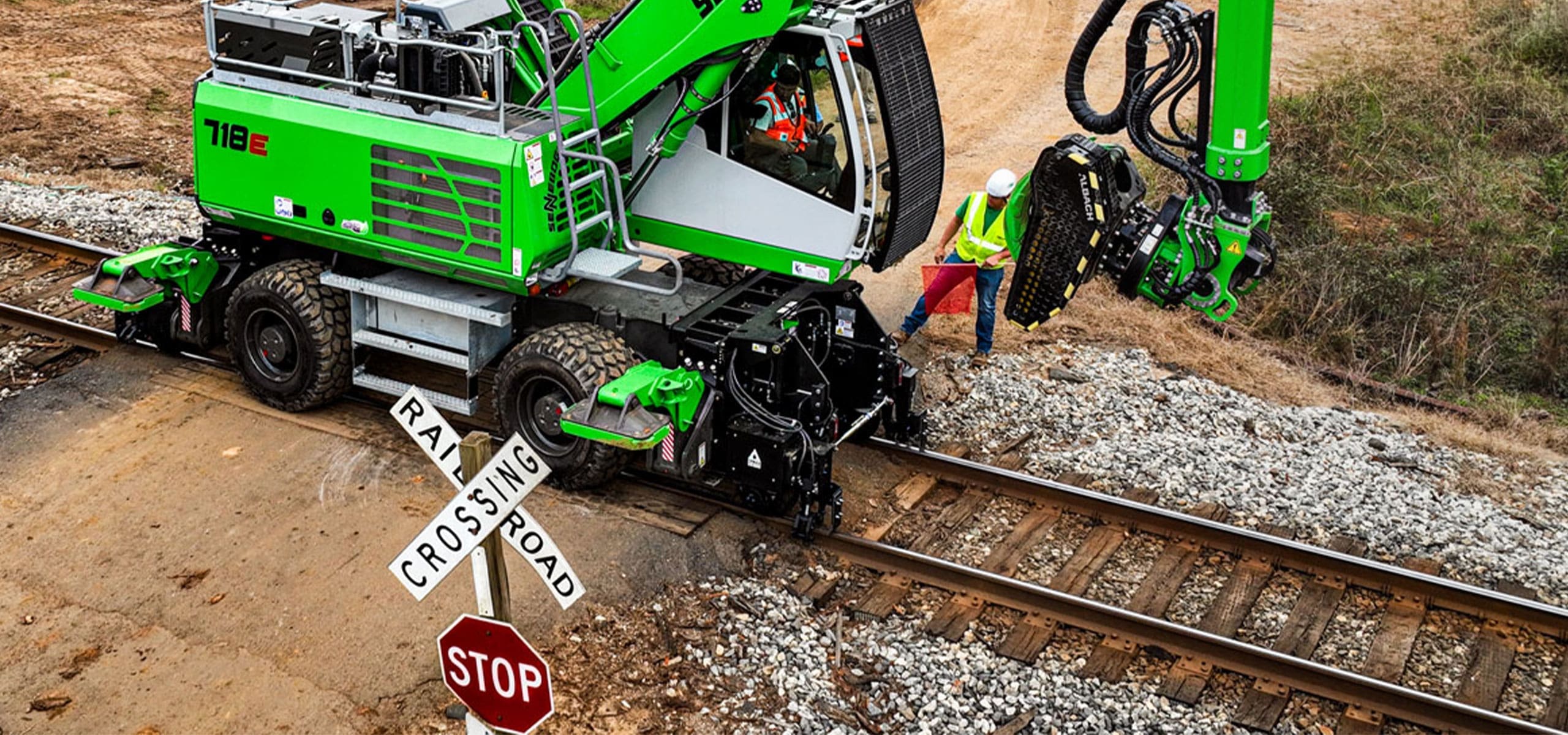 Sennebogen 718 wheel excavator equipped with Dymax Rail Rider WX4S hi-rail system, traveling on track at a railroad crossing.