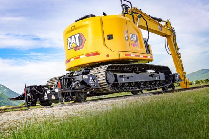 Cat 315 track excavator equipped with the Dymax Rail Rider X2-15T detachable hi-rail attachment on rail, shown from the rear with the modular hi-rail assemblies fully supporting the machine