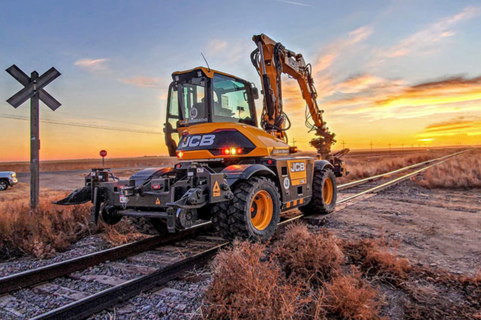 Hi-rail wheel excavator on rails at sunset Wheel excavator equipped with DymaxRail Rail Rider WX hi-rail guidance system operating on railroad track